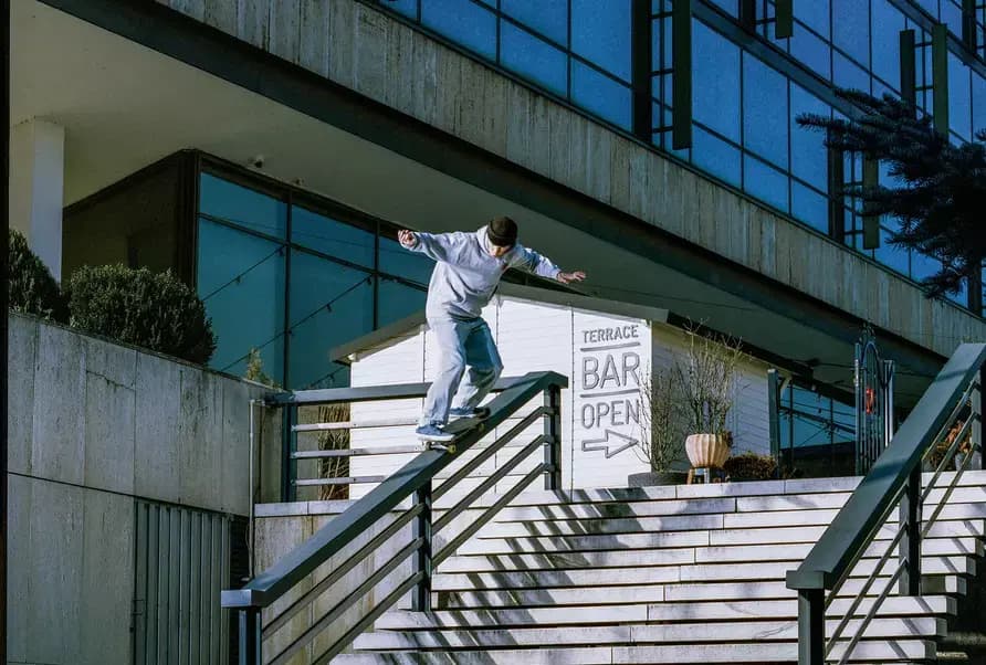 A top-down view of a skateboarder preparing to perform a trick down a staircase while a cameraman films from below.